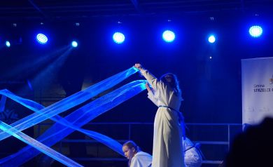 Taniec z chustą dziewcząt ubranych w białe suknie. Scenę oświetla niebieskie światło. 