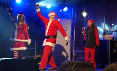 Występ dwóch kobiet i mężczyzny na scenie. Przebrani są w świąteczne stroje, m.in. w strój Mikołaja. 