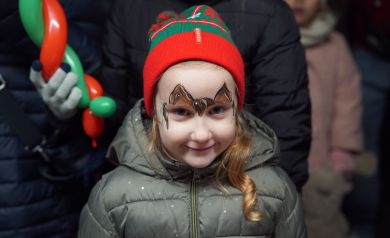 Dziewczynka w czerwono-zielonej czapce z pomalowaną twarzą. 