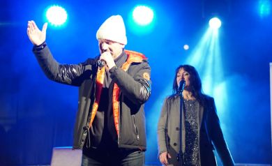 Występ Damiana Holeckiego. Za artystą stoi kobieta i śpiewa do mikrofonu. 