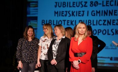 Na zdjęciu kilka uśmiechniętych kobiet. W tle wyświetlana jest prezentacja. 