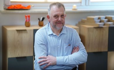 Mężczyzna w lekkim zaroście i niebieskiej koszuli. Ręce ma założone na piersiach.