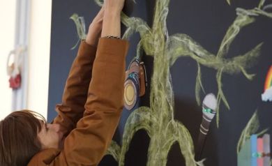 Kobieta mocująca nadrukowane nuty na kartce na drzewo namalowane na czarnej tablicy.