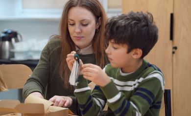 Na zdjęciu kobieta mająca długie brązowe włosy i chłopiec w pasiastym swetrze wykonują ozdobę - skrzaty.