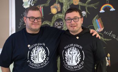 Dwóch mężczyzn ubranych w koszulki z logiem Klubu Gier Planszowych w Strzelcach Opolskich.