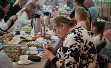 Kobieta pochylona ze skupieniem w trakcie pracy. Widać już wiele dokończonych prac na stole.