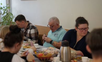 Mężczyzna pośrodku pracujący nad kroszonką, w tle reszta ludzi w ferworze pracy