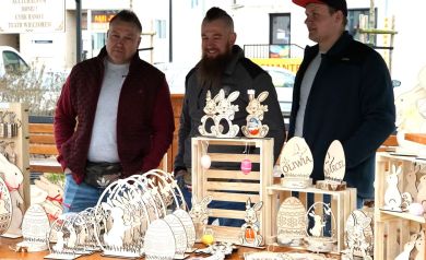 Trzech panów stoi i sprzedaje ozdoby świąteczne ze sklejki, na stole są jajka, zające wielkanocne.