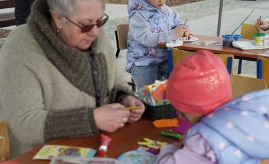 Pani ze świetlicy pomaga dziewczynce dekorować żółtego zajączka wielkanocnego.