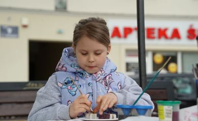 Dziewczynka w błękitnej  kamizelce, maluje gipsowe jajeczka