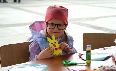 Dziewczynka uczestniczy w zajęciach plastycznych na jarmarku, stworzyła żółtego króliczka.