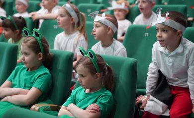 dzieci przebrane za żabki siedzą na fotelach sali widowiskowej