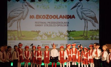 dziewczynki i chłopcy przebrane w sukienki ludowe i wianki na scenie sali widowiskowej