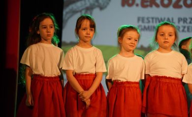 dziewczynki przebrane w czerwone sukienki i białe koszulki na scenie sali widowiskowej