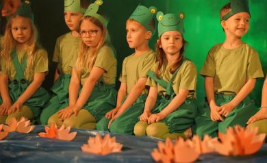 dzieci przebrane za żabki siedzą na scenie