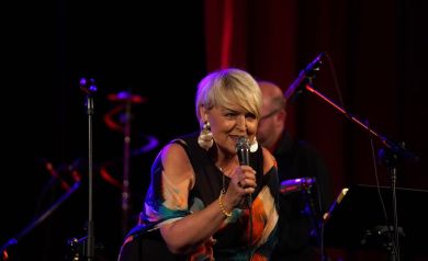 Śpiewająca Krystyna Stańko nachyla się z uśmiechem w kierunku publiczności