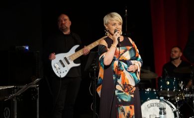 Na pierwszym planie śpiewająca wokalistka, w oddali grający basista i perkusista