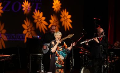 Scena z oddali z pełnym składem muzyków, w tle wirują kwiatowe wzory