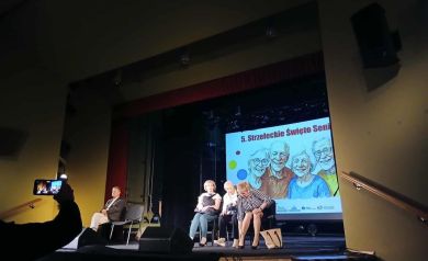 Na scenie występ grupy teatralnej. W tle wyświetlana jest grafika związana z 5. Strzeleckim Świętem Seniorów.