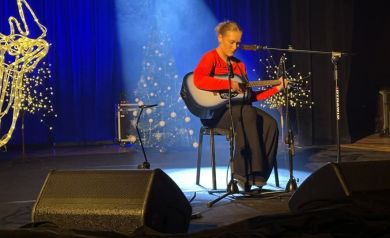 Artystka grająca na gitarze znajduje się na scenie, gra świąteczne kolędy 