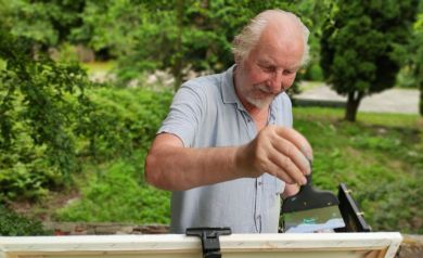 Artysta Leszek Gapski nakłada farbę szpachlą na płótno.