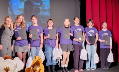 Zdjęcie grupowe uczestników projektu ,,Równać Szanse' -  „Młodzieżowo Strzelecko Redaktorski Zawrót Głowy”. Znajdują się na scenie, w ich dłoniach czarne teczki oraz białe worki z upominkami. 