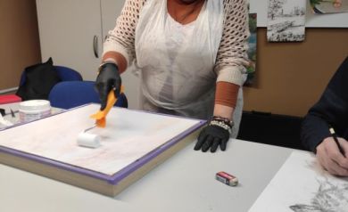 Zdjęcie przedstawia kobietę malującą małym wałkiem obraz. 