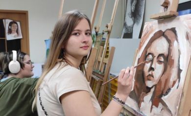 Na zdjęciu dziewczyna malująca obraz stojący na sztaludze. 