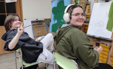 Młodzież uśmiechająca się do zdjęcia. Przed nimi sztalugi z obrazami. 