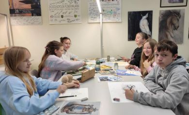 Dzieci i młodzież pracująca przy stole nad swoimi pracami. 