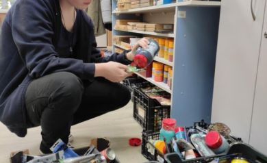 Osoba biorąca udział w zajęciach . Nakłada farbę na tackę. Wokół niej w skrzynkach farby, bądź inne materiały potrzebne na zajęcia. 