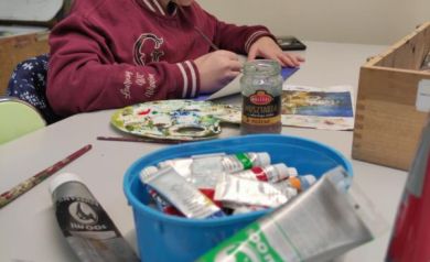 Na zdjęciu dziewczynka malująca swoje dzieło. Widać farby oraz inne potrzebne materiały do przeprowadzenia zajęć. 