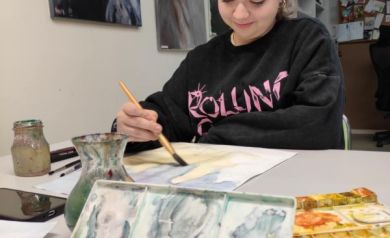 Dziewczyna pracująca nad swoim dziełem. W dłoni trzyma pędzel, którym maluje. 