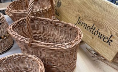 Na zdjęciu widać ręcznie plecione kosze z wikliny ustawione na stole, obok drewnianej tablicy z napisem „Pracownia Wikliniarska – Jarnołtówek”. 