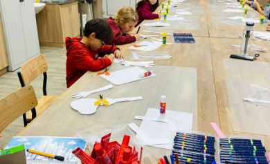 Stół z przyborami do wykonywania dzieł plastycznych oraz dzieci wykonujące swoje prace. 