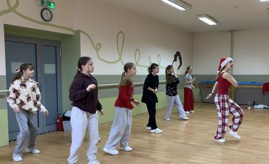 Zdjęcie przedstawia grupę młodych ludzi, dziewcząt, uczestniczących w zajęciach tanecznych w sali tanecznej. Jedna z kobiet ma na głowie świąteczną czapkę.