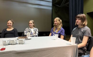 Na zdjęciu cztery dziewczyny siedzące przy stole, na którym znajdują się filiżanki, kubki na wodę oraz ciasteczka na talerzu. 